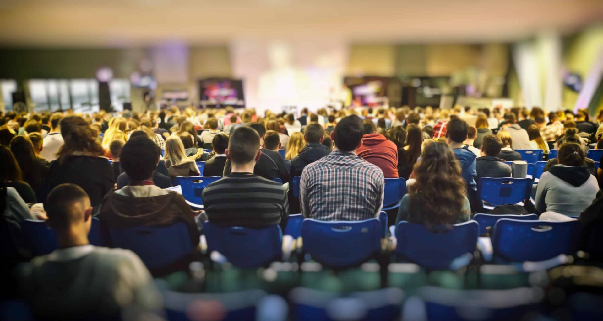 A lot of young people in a big hall listening to a speaker