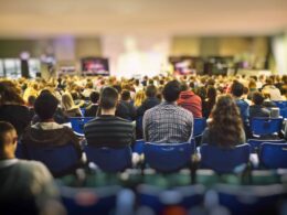 A lot of young people in a big hall listening to a speaker